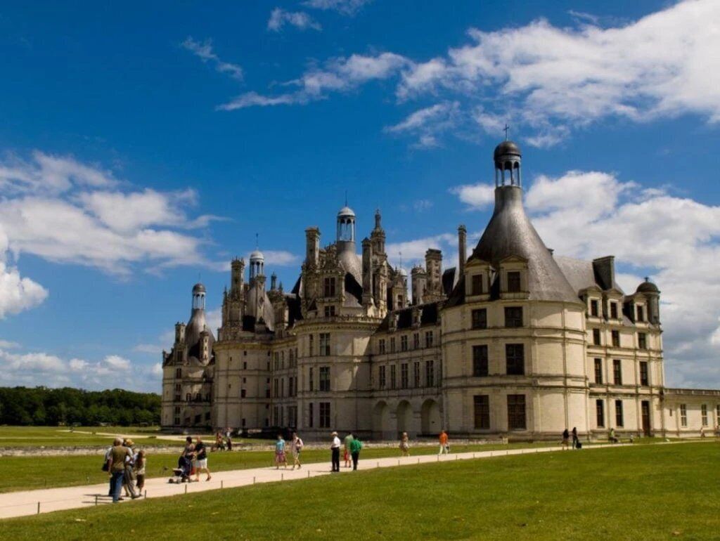 A historic building with multiple towers and a large lawn area.