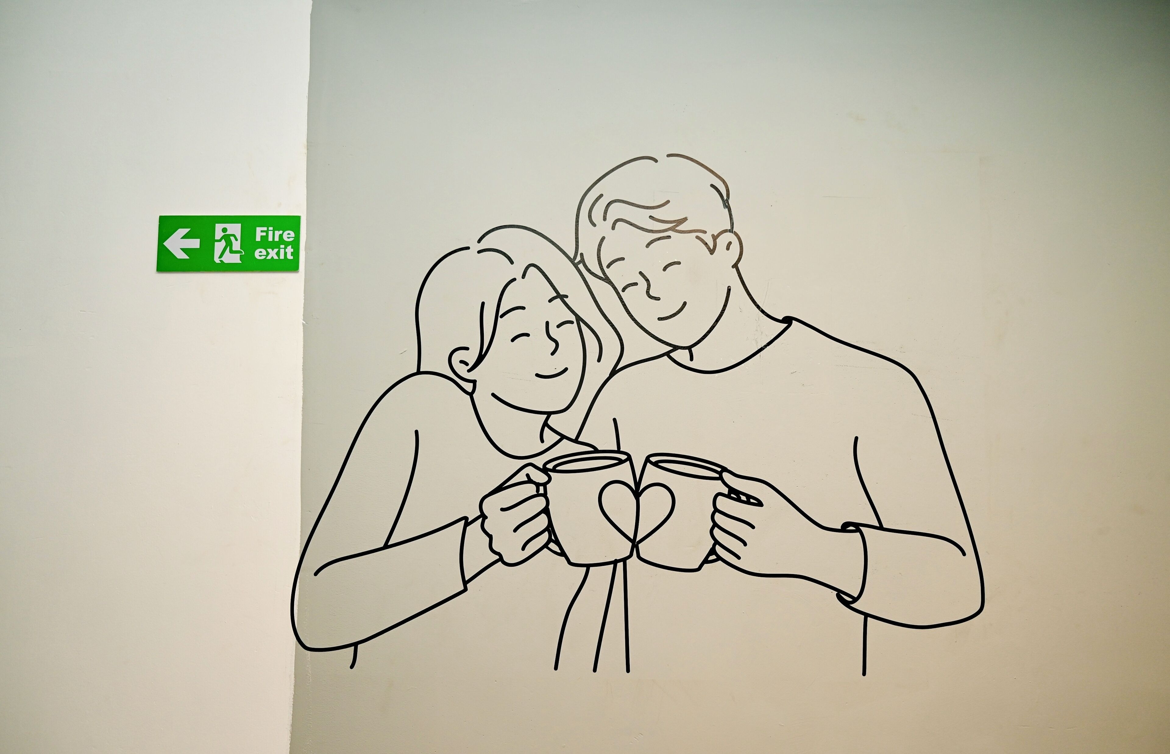A line drawing of two people holding mugs, with a fire exit sign in the background.