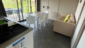 Una cocina moderna con estufa integrada, una zona de comedor con sillas blancas y un sofá color beige.