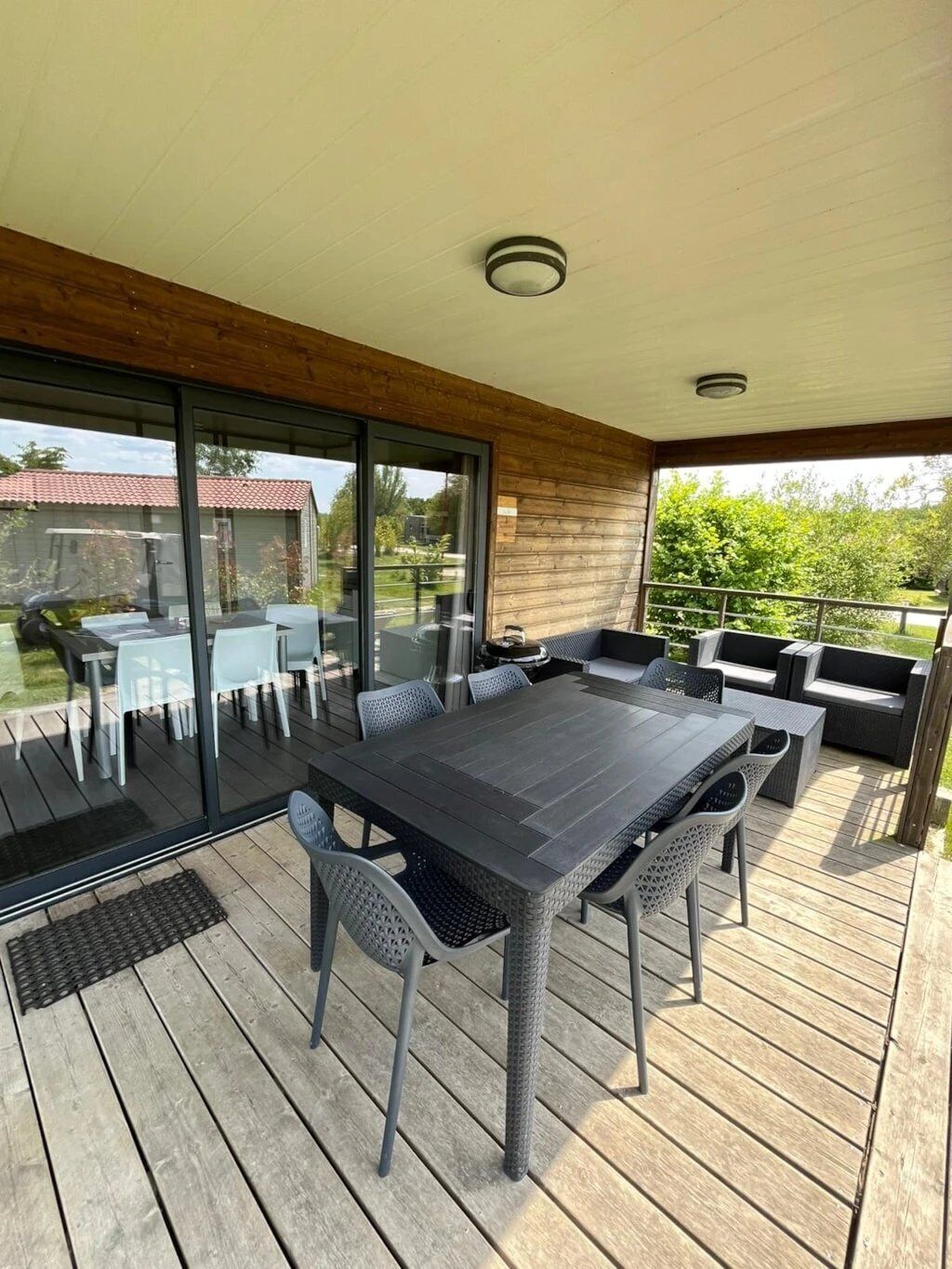 A covered outdoor patio with a dining table and chairs, a seating area with sofas, and a view of the surrounding landscape.