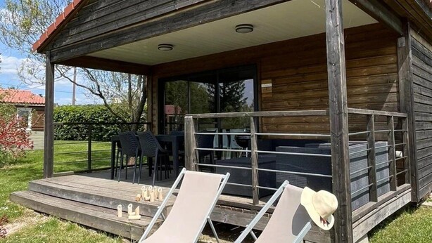 Una cabaña de madera con un porche cubierto, dos sillones de descanso y una mesa con sillas.