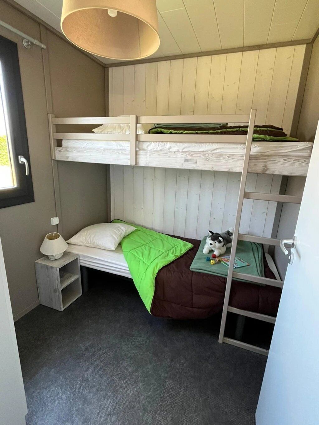Habitación pequeña con literas, una mesita de noche, una lámpara y un juguete en la litera inferior.