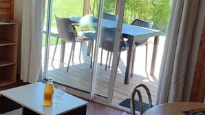 A cozy room with a wooden ceiling, a sliding glass door leading to an outdoor patio, a small table with a bottle and glasses, and a bench.
