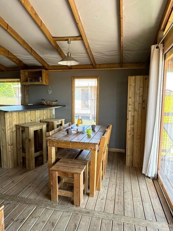 A rustic wooden interior with a dining table and benches, a window with blinds, and a wooden ceiling structure.