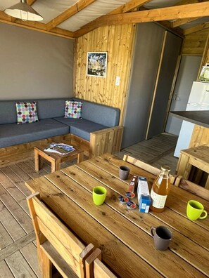 A cozy cabin interior with a wooden dining table, a sofa with colorful cushions, and a kitchen area.