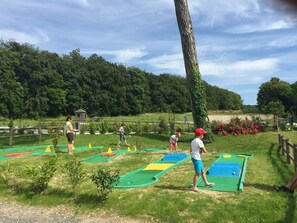 A golf course with multiple putting greens, a wooden fence, and a backdrop of dense trees.