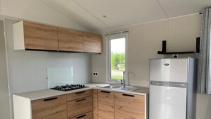 A compact kitchen with wooden cabinets, a white countertop, a gas stove, a sink, and a refrigerator. - ZEcamping 3 étoiles familial piscine chauffée locatif TV BBQ 32m2 (Grand-Laviers)