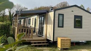 A single-story mobile home with a porch and a small deck, surrounded by greenery. - ZEcamping 3 étoiles chiens acceptés animations piscine chauffée (Grand-Laviers)