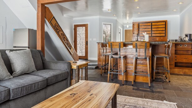 Une cuisine moderne avec des tabourets de bar en bois, un îlot central et un escalier menant à un autre niveau.