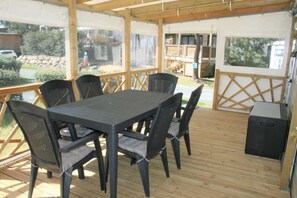 Une terrasse couverte avec une table et des chaises, un barbecue et un haut-parleur.