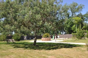 A park with a bench, a playground, and a large tree. - ZEcamping 4* piscine couverte 2km plage animations locatif TV LV 40m2 (Saint-Hilaire-de-Riez)