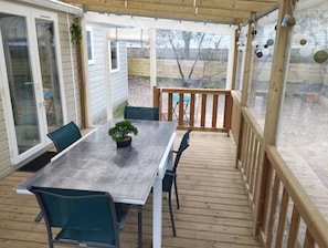 Une terrasse couverte avec une plateforme en bois, une table et des chaises, et un pot de fleurs.