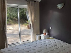 Ein Schlafzimmer mit großem Fenster, einem Bett, einem Nachttisch und einer Wandlampe.