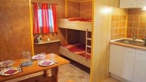 Quarto compacto com beliche, pequeno espaço de cozinha e mesa de jantar com pratos e copos.
