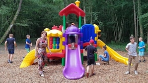 A playground with a slide and climbing structures surrounded by trees. - ZEcamping 4* familial piscine dog friendly locatif TV BBQ 35m2 7 pers (La Bastide-de-Sérou)