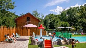 A wooden cabin with a pool area, including a slide and lounge chairs. - ZEcamping 4* familial piscine dog friendly locatif TV BBQ 35m2 7 pers (La Bastide-de-Sérou)