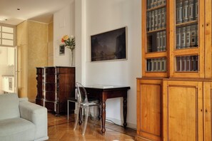 A room with a wooden desk, a chair, a cabinet with books, and a painting on the wall. - JOIVY Airy flat near the city centre (Milan)