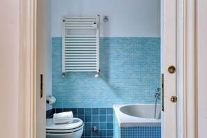A bathroom with a toilet, a towel rack, and a bathtub. - JOIVY Airy flat near the city centre (Milan)