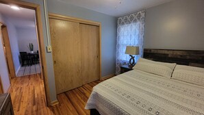 Camera da letto con porta in legno, un letto con copriletto decorato, un comodino con lampada e una finestra con tende a motivi.