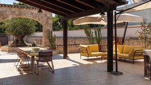 Une terrasse extérieure agrémentée d’une arche en pierre, d’une table avec des chaises et d’un canapé jaune placé sous une pergola.