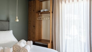 Une chambre avec une armoire en bois, un lit avec du linge de lit blanc et un luminaire suspendu.