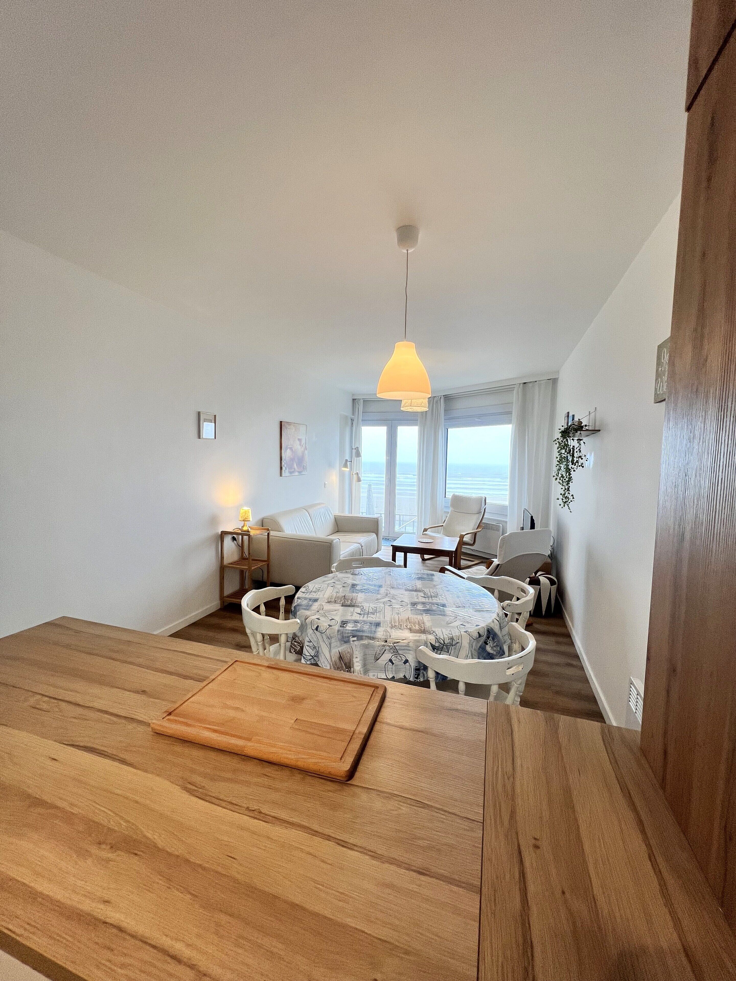Un salon moderne avec une table à manger en bois, des chaises blanches, un canapé et un luminaire suspendu.