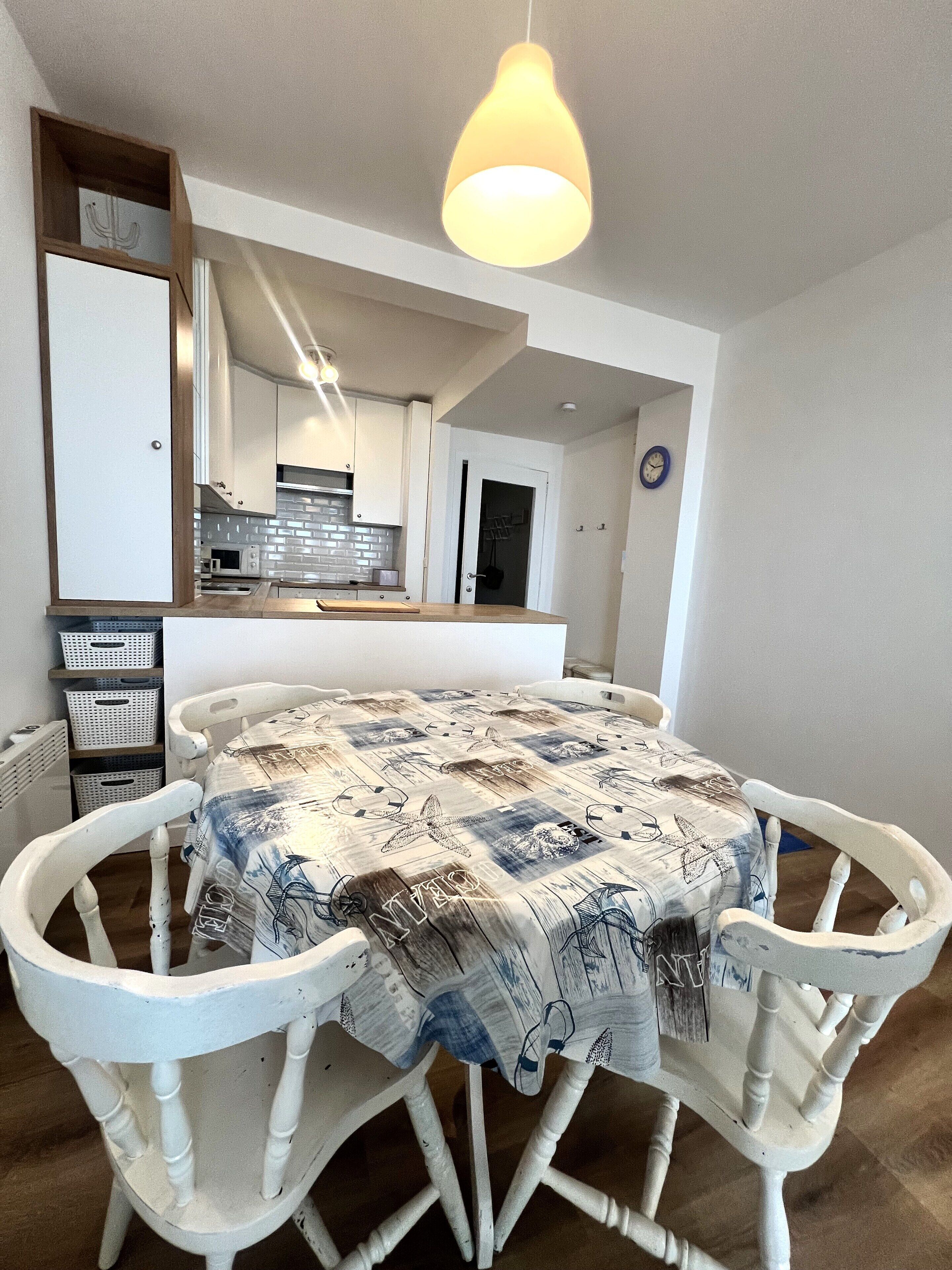 A dining area with a round table, white chairs, and a patterned tablecloth.