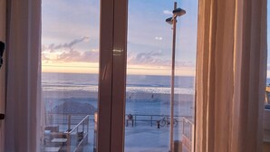 Una habitación con un amplio ventanal corredizo que da a un balcón con vistas al mar y al atardecer.