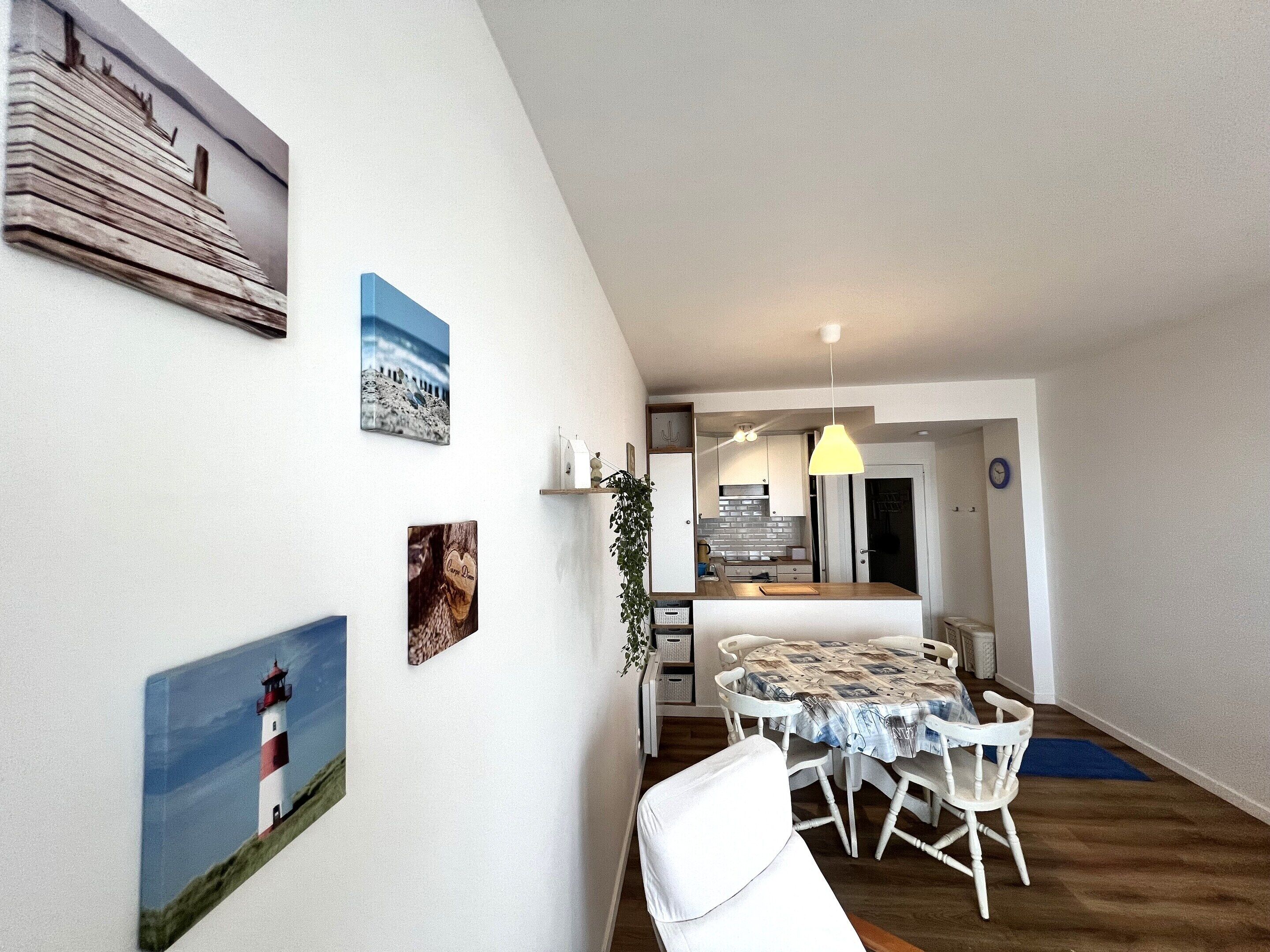 A modern kitchen with white cabinets, a built-in oven, and a dining area with a round table and white chairs.