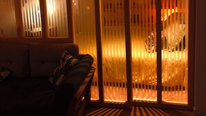 Een kamer met een bank, een houten bankje en een glazen schuifdeur met verticale jaloezieën.