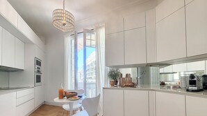 A modern kitchen with white cabinetry, a dining table with chairs, and a view of the city through the window.