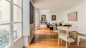 A spacious room with a wooden floor, a dining area with a table and chairs, and a large window providing a view of the outside. - Magnificent duplex in the Marais district (Paris)