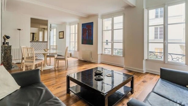 A spacious living room with a black coffee table, wooden flooring, and large windows offering views of the outside. - Magnificent duplex in the Marais district (Paris)