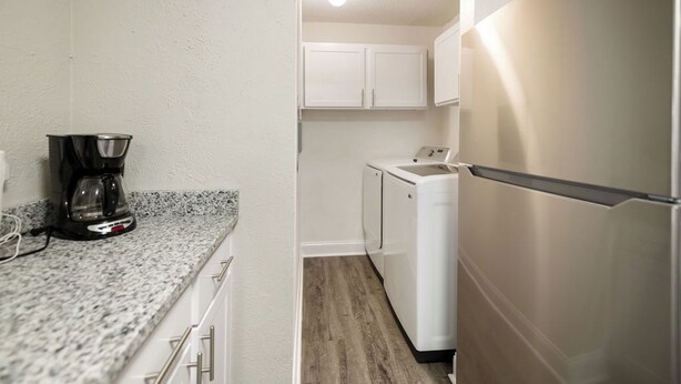 A compact kitchen with a coffee maker, a washing machine, and a refrigerator.