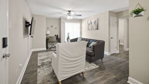 A living room with a ceiling fan, a gray sofa, a white chair, and a gray rug.
