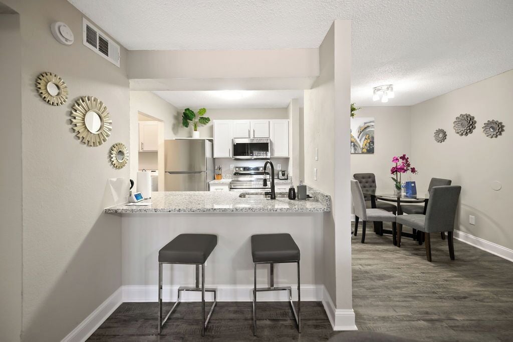 A modern kitchen with a central island, bar stools, and a dining area with a table and chairs.