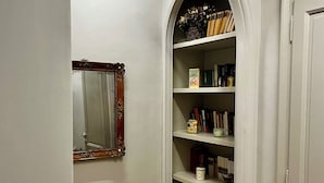 Un passadís estret amb terra de fusta, una porta blanca, una paret blanca i una estanteria plena de llibres i objectes decoratius.