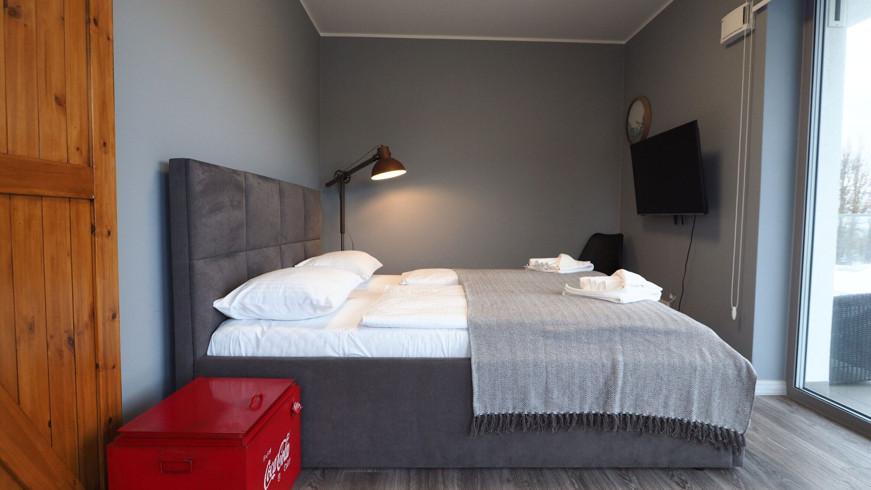 Un dormitorio con cama, televisión, ventana y un refrigerador rojo de Coca-Cola.