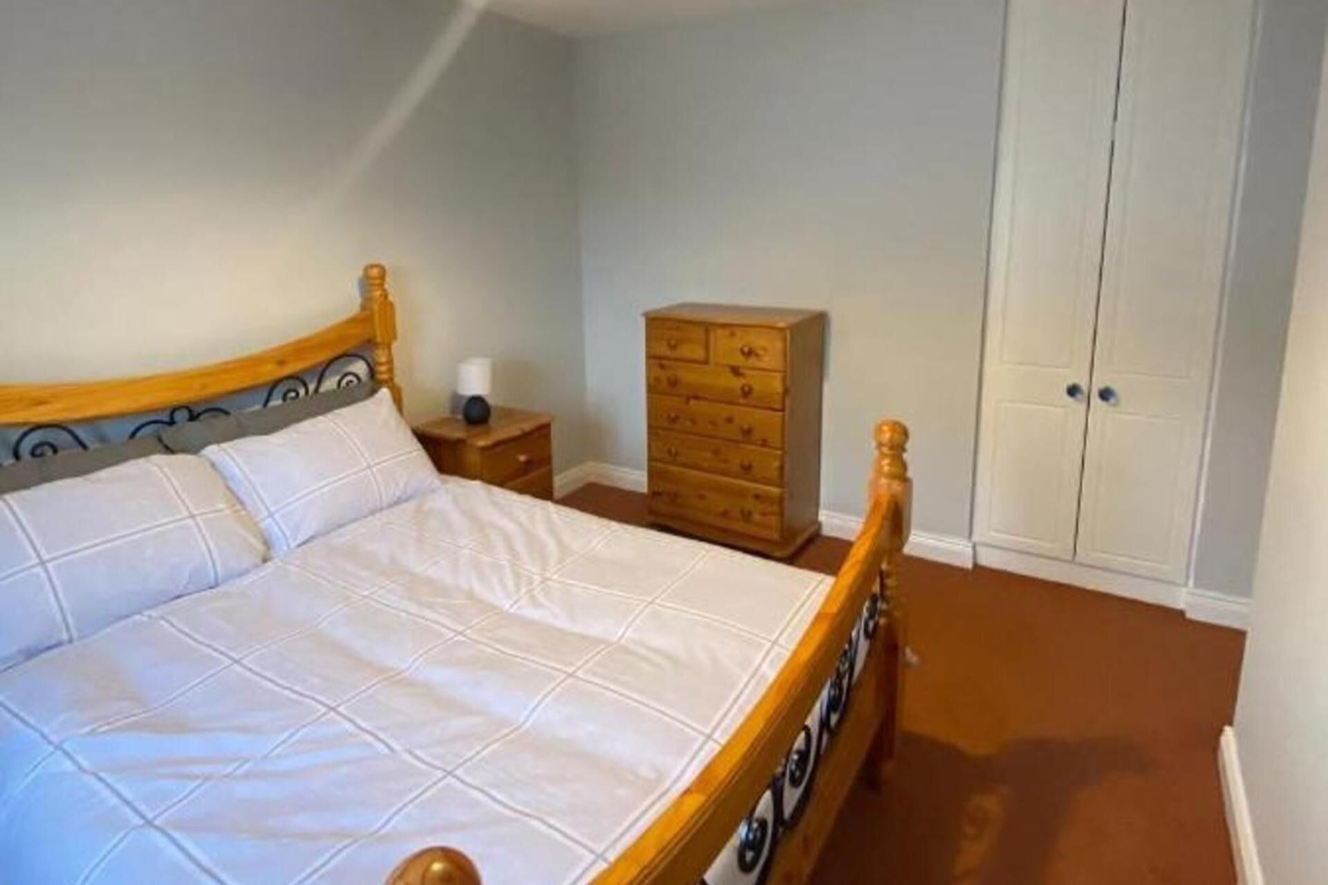 A bedroom with a wooden bed, a nightstand, a dresser, and a wardrobe.