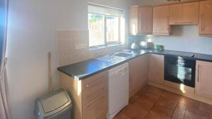 A compact kitchen with a dishwasher, a sink, and wooden cabinets. - 3 Bed-sleeps 5-garden-parking-pets (Dromahair)
