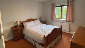 A bedroom with a wooden bed, a nightstand, a dresser, and a window with curtains. - 3 Bed-sleeps 5-garden-parking-pets (Dromahair)