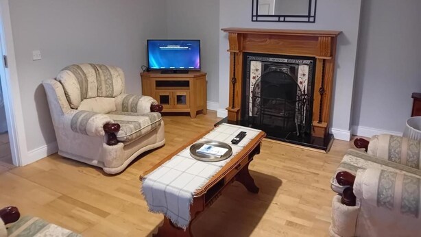 A living room with a wooden floor, a beige armchair, a television on a wooden stand, and a fireplace with a decorative mantel. - 3 Bed-sleeps 5-garden-parking-pets (Dromahair)