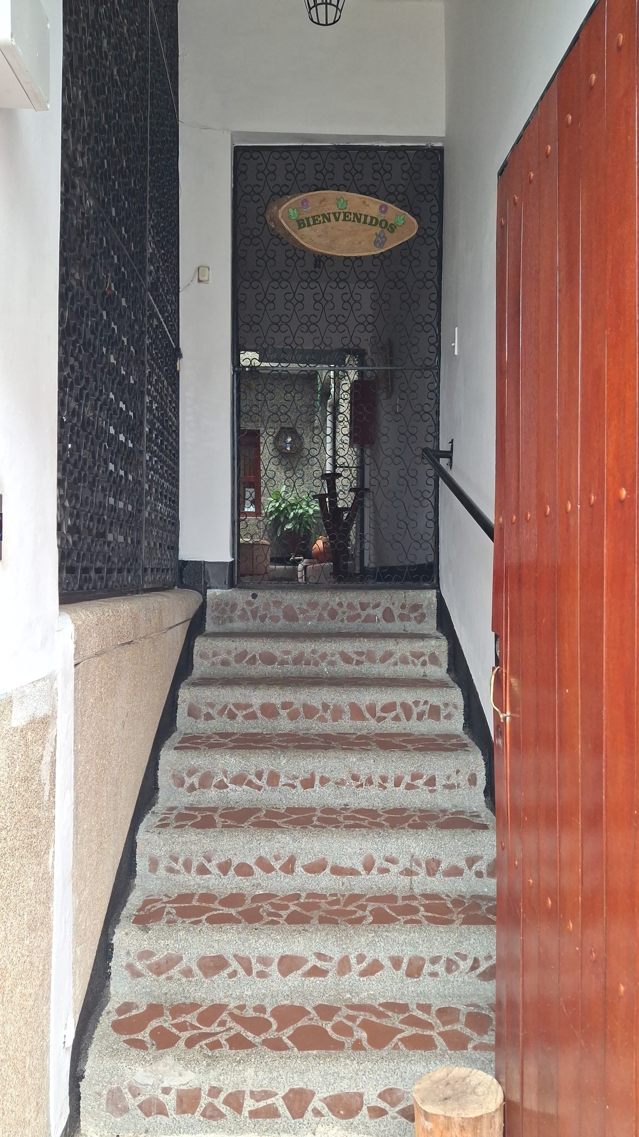 Una escalera conduce a un espacio con un cartel de 'BIENVENIDO', una puerta de madera y vistas a un jardín.