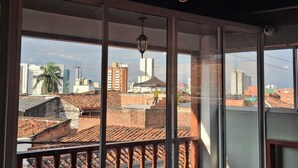 Vista desde un balcón con un paisaje urbano de fondo, que incluye edificios modernos y antiguos, bajo un cielo despejado.
