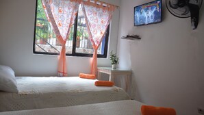 Un dormitorio con dos camas, una ventana con cortinas, un televisor en la pared y un ventilador.