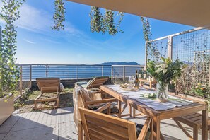 A terrace with wooden furniture, a table set with a vase of flowers, and a view of the sea. - Aurora Apartment by Rent all Como (Como)