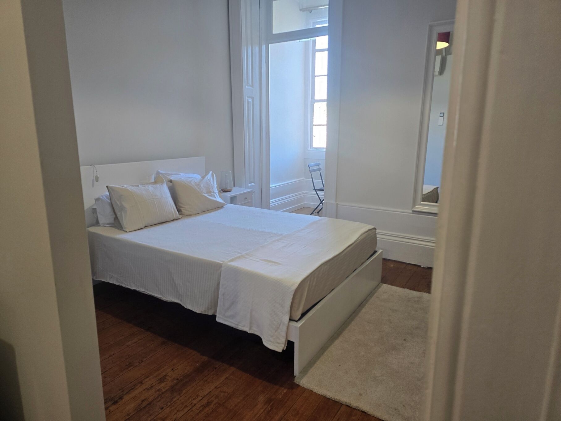 A bedroom with a bed, a nightstand, a window, and a door.