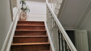 Eine Holztreppe mit weißen Wangen führt zu einer Zwischenebene. Ein gerahmtes Stadtbild hängt an der Wand darüber.
