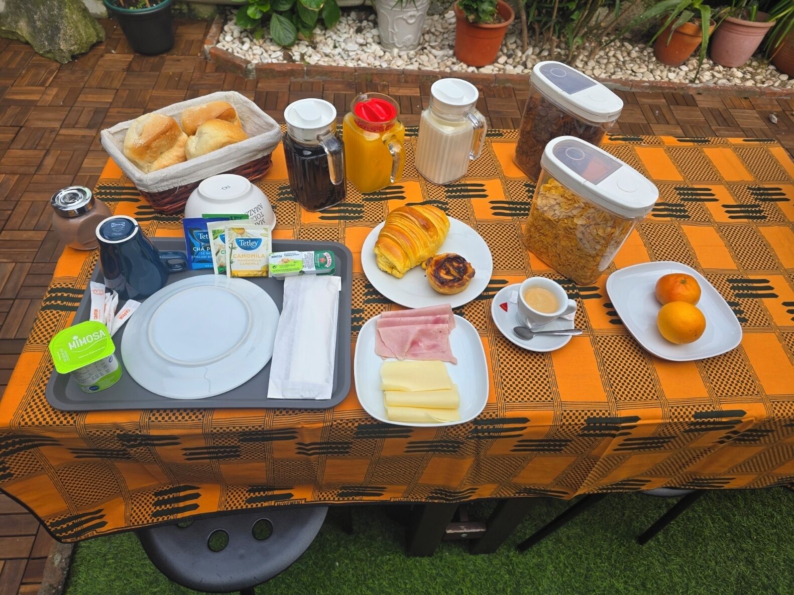 Een ontbijt met brood, gebak, koffie en fruit op een buitentafel.