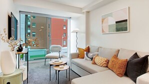 Una sala de estar moderna con un juego de sofá, una mesita y un sillón. Hay un ventanal con vistas a edificios.